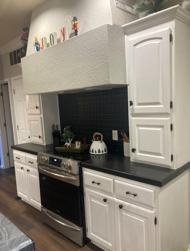 kitchen featuring backsplash, stainless steel range with electric stovetop, dark wood-type flooring, exhaust hood, and white cabinetry