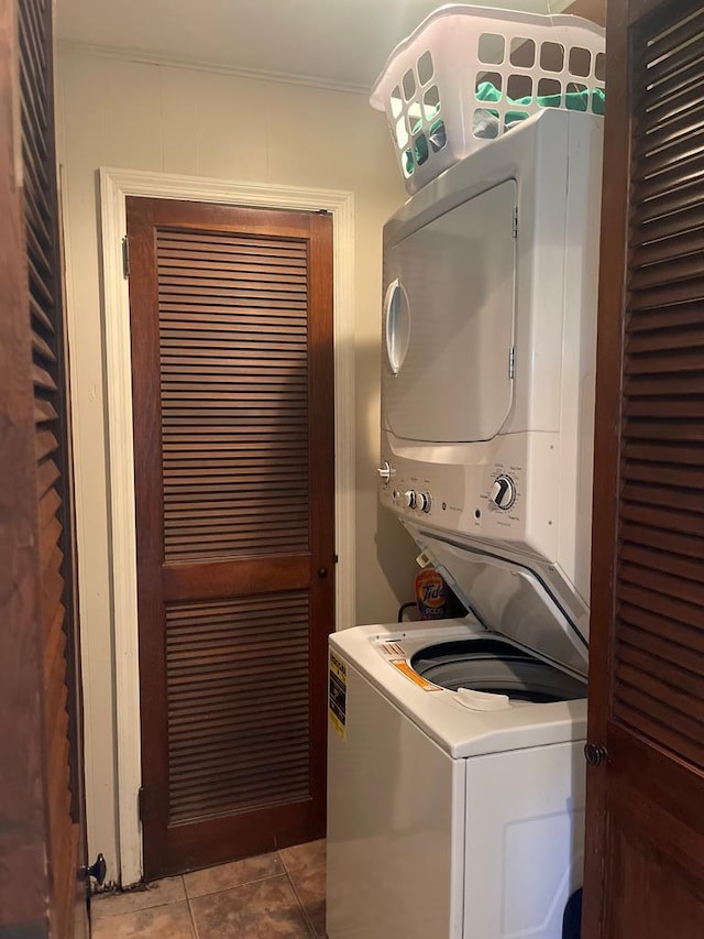laundry area featuring ornamental molding, tile patterned flooring, stacked washing maching and dryer, and laundry area
