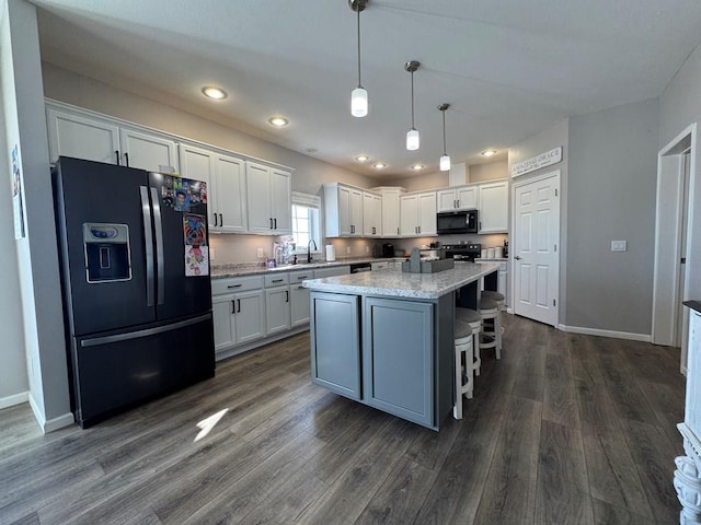 kitchen with pendant lighting, a center island, light stone counters, black appliances, and white cabinets