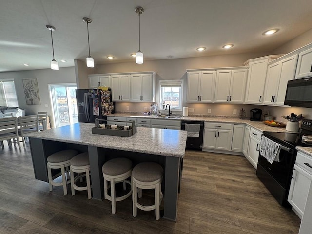 kitchen with pendant lighting, black appliances, a center island, and white cabinets