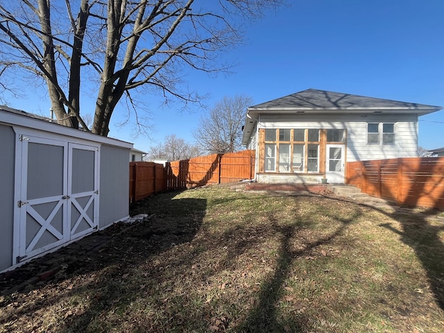 rear view of house featuring a storage unit, a yard, an outbuilding, and a fenced backyard