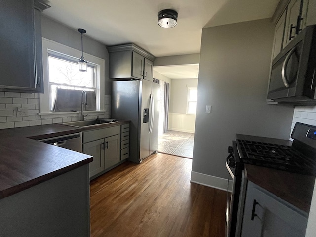 kitchen with dark wood-style floors, a sink, appliances with stainless steel finishes, dark countertops, and backsplash