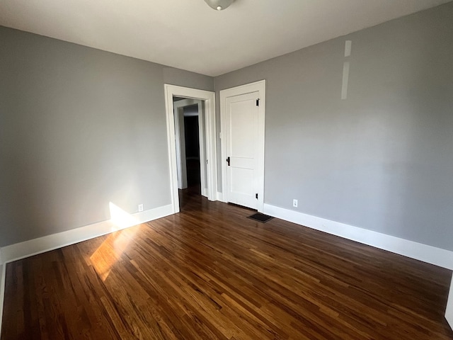 unfurnished room with visible vents, baseboards, and dark wood-style flooring