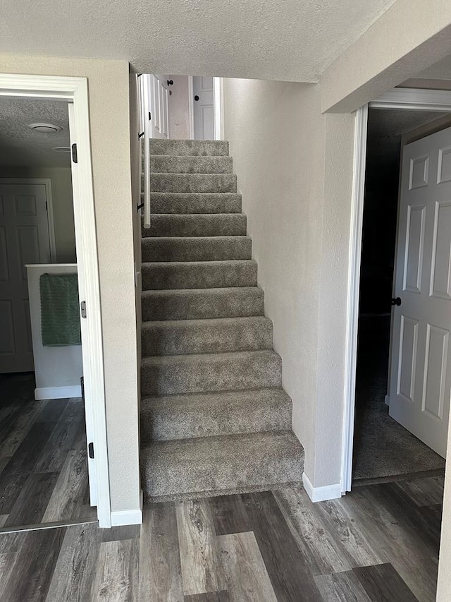 stairway with wood-type flooring and a textured ceiling