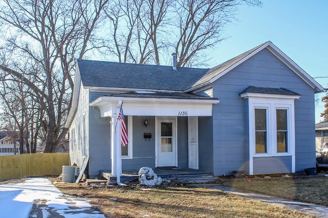 bungalow with a shingled roof, fence, central AC unit, and a porch