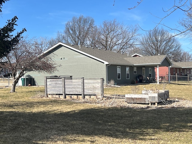 back of property with a lawn, a shingled roof, and fence