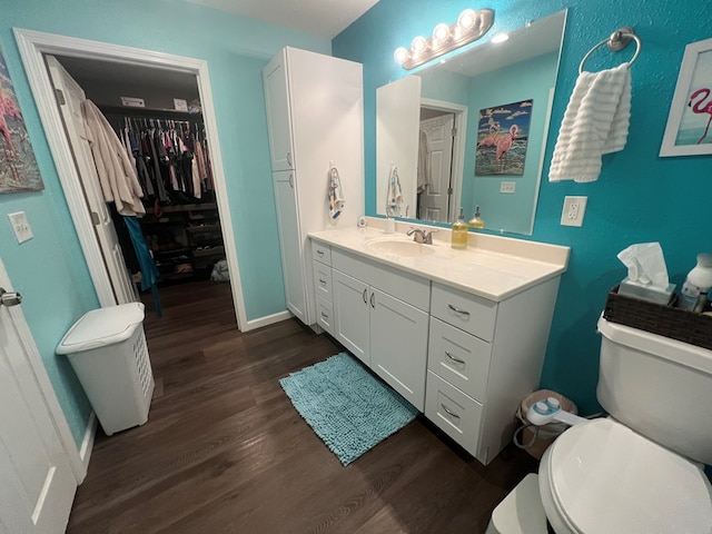 bathroom featuring a walk in closet, toilet, wood finished floors, baseboards, and vanity