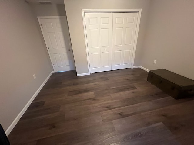 unfurnished bedroom featuring baseboards, dark wood-style flooring, and a closet