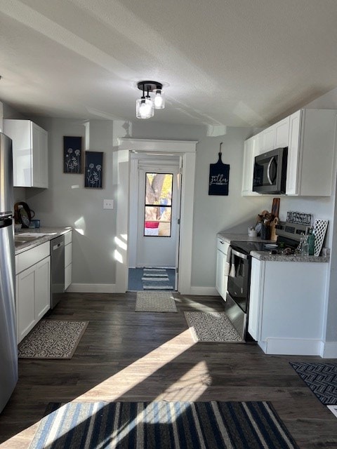 kitchen with stainless steel appliances, white cabinetry, and dark hardwood / wood-style floors