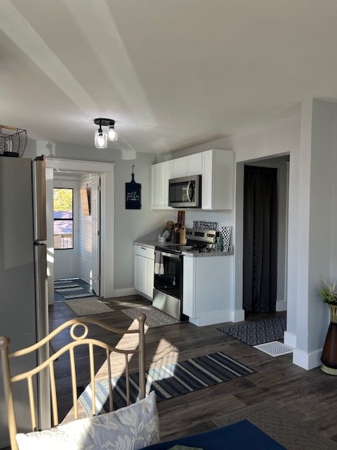 kitchen featuring stainless steel appliances, white cabinetry, dark hardwood / wood-style floors, and dark stone counters