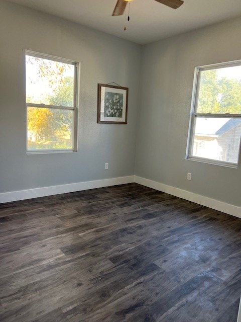 empty room featuring ceiling fan, dark wood-type flooring, and a healthy amount of sunlight