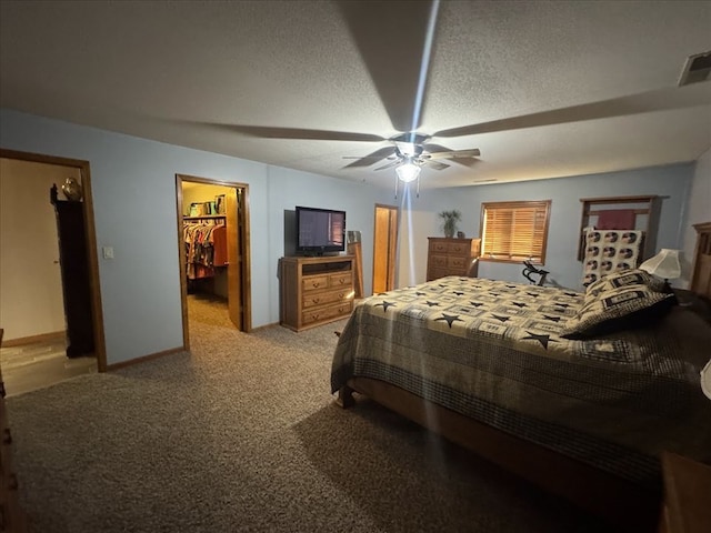 carpeted bedroom with ceiling fan, a walk in closet, a closet, and a textured ceiling