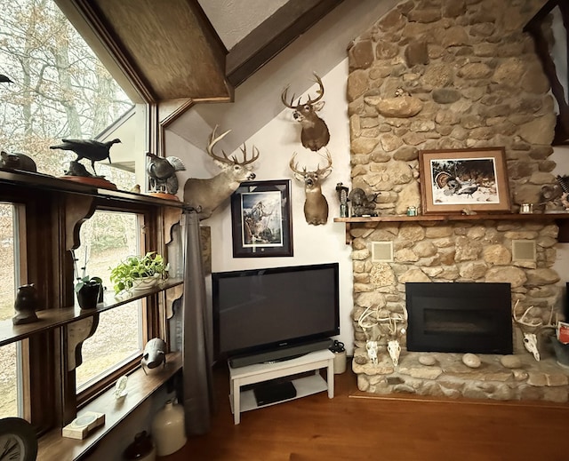 interior space with a stone fireplace, vaulted ceiling with beams, and hardwood / wood-style flooring