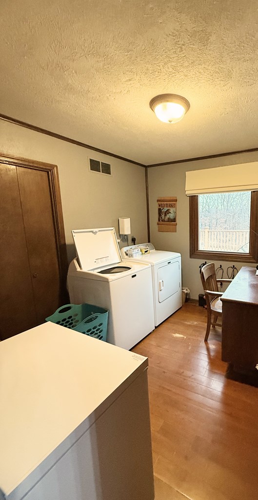 clothes washing area featuring light wood-type flooring, a textured ceiling, and independent washer and dryer