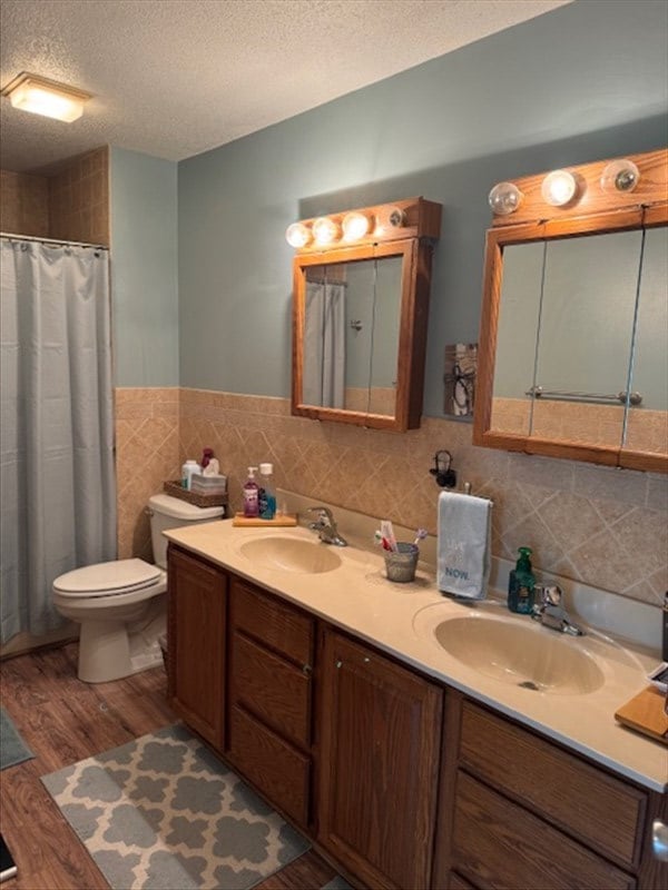 34829 State Highway C, Bevier, MO 63532 - bathroom with a textured ceiling, wood finished floors, double vanity, tile walls, and wainscoting