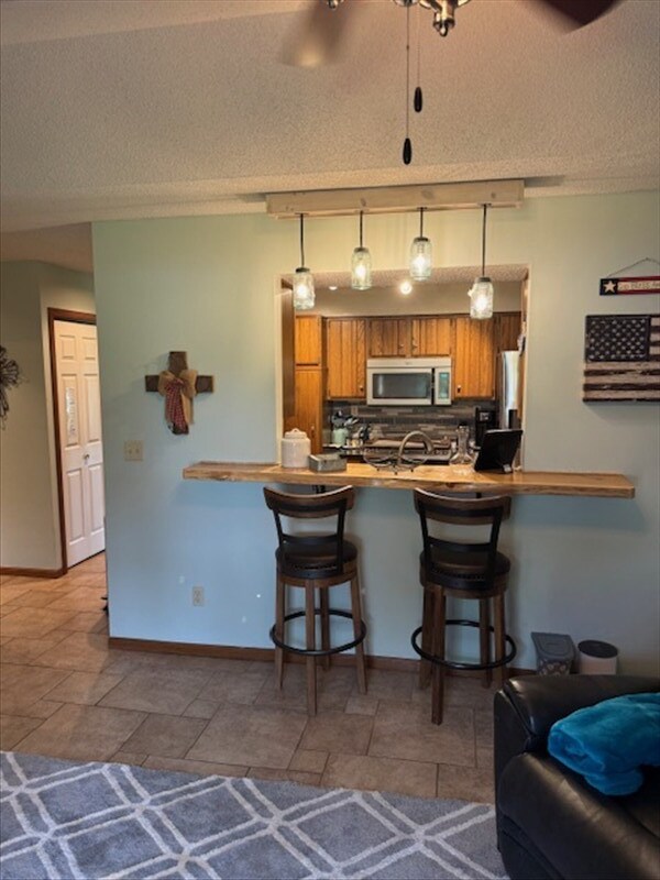 34829 State Highway C, Bevier, MO 63532 - kitchen featuring stainless steel appliances, a peninsula, a kitchen breakfast bar, brown cabinets, and a textured ceiling