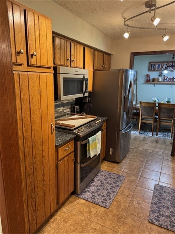 34829 State Highway C, Bevier, MO 63532 - kitchen with stainless steel appliances, brown cabinets, decorative backsplash, rail lighting, and a textured ceiling