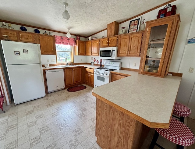 kitchen with a sink, ornamental molding, white appliances, and brown cabinets