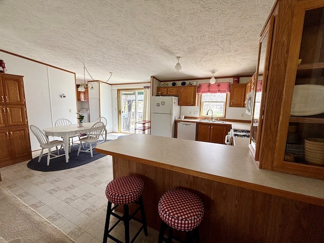 kitchen featuring a sink, white appliances, a peninsula, brown cabinets, and crown molding