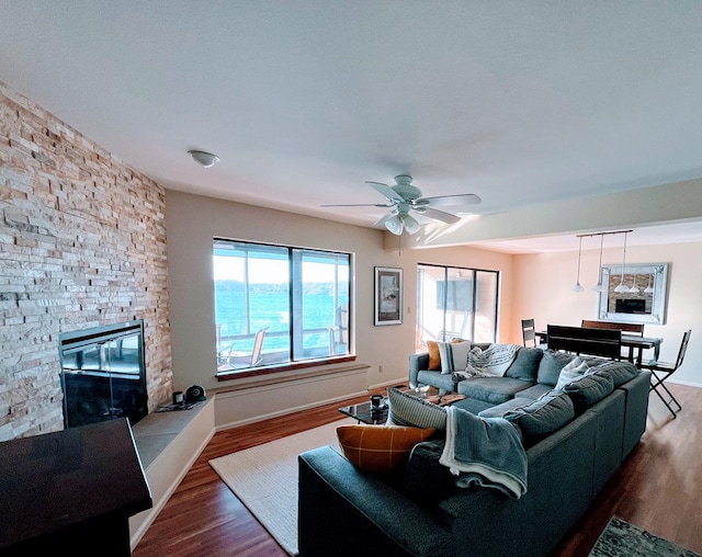 living room featuring a water view, ceiling fan, a stone fireplace, and hardwood / wood-style floors