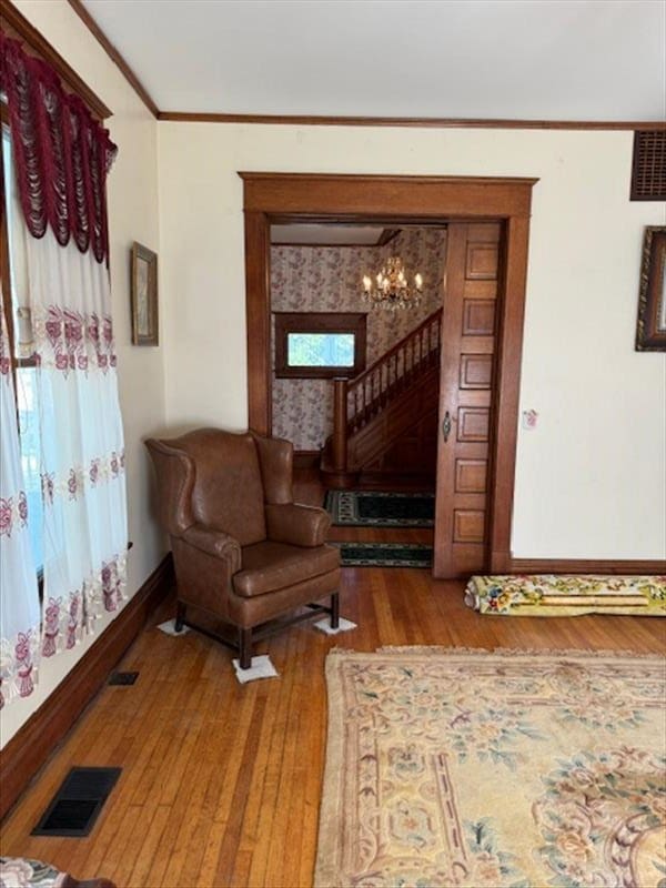 living area with hardwood / wood-style flooring, ornamental molding, and an inviting chandelier