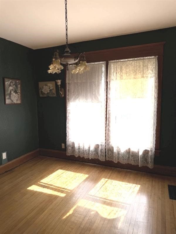 spare room featuring hardwood / wood-style floors, a notable chandelier, and a healthy amount of sunlight