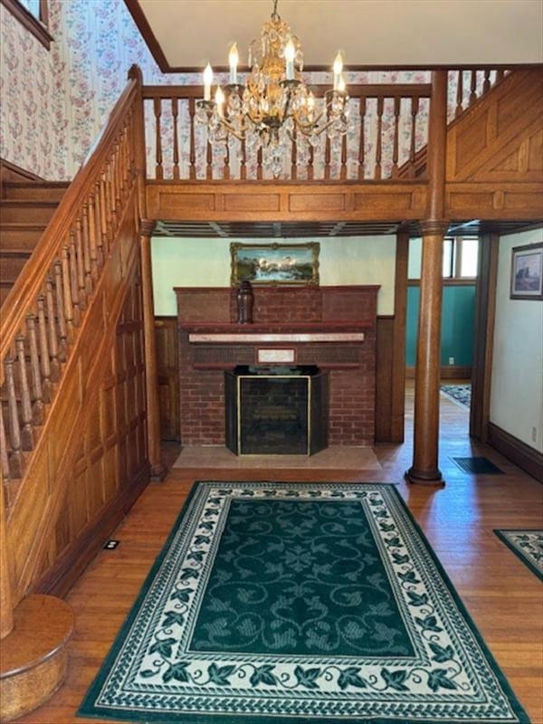 living room featuring ornate columns, hardwood / wood-style flooring, a notable chandelier, and a brick fireplace