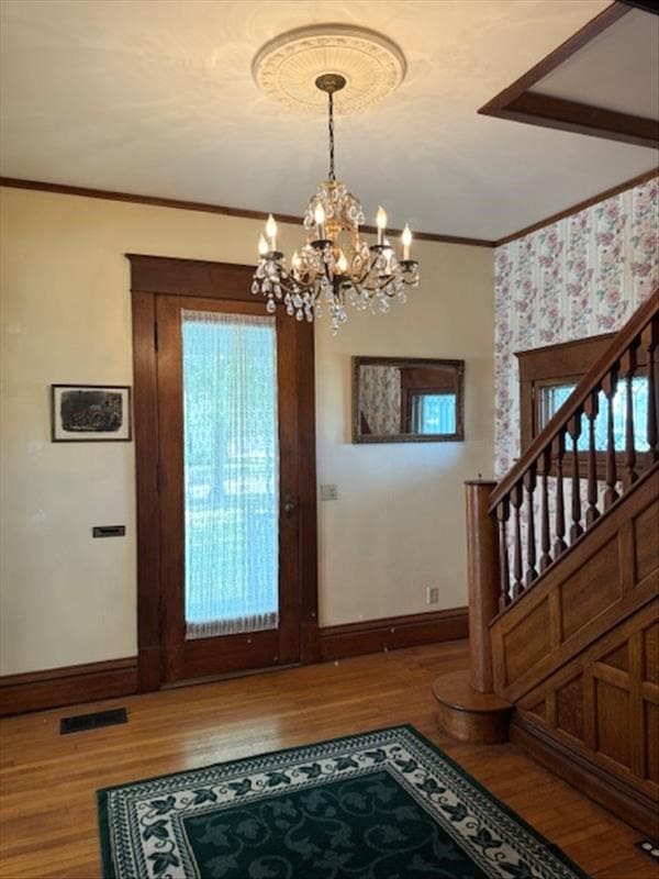 entrance foyer with hardwood / wood-style floors, crown molding, and a chandelier