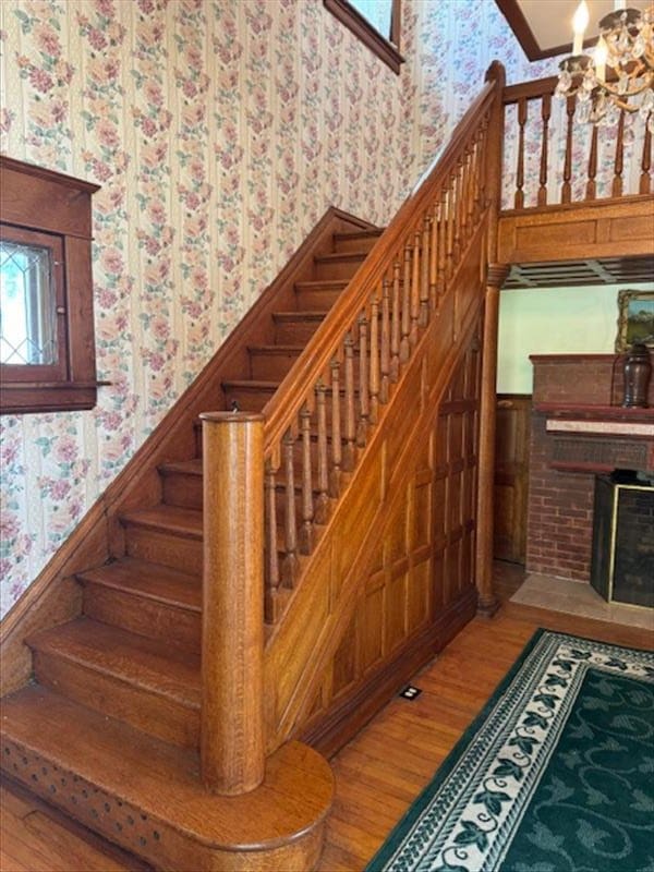 stairway featuring a chandelier, wood-type flooring, and a brick fireplace