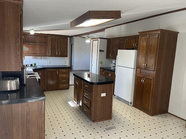 kitchen featuring light floors, freestanding refrigerator, ceiling fan, dark countertops, and a center island