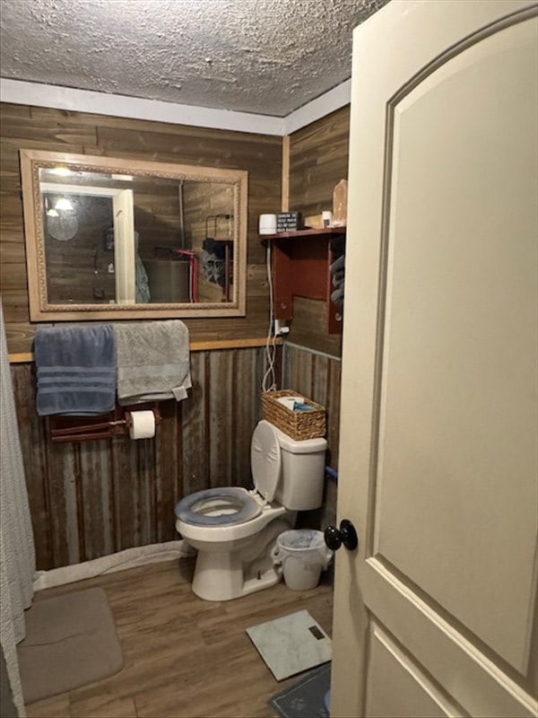 bathroom with a textured ceiling, wood walls, wood finished floors, and toilet