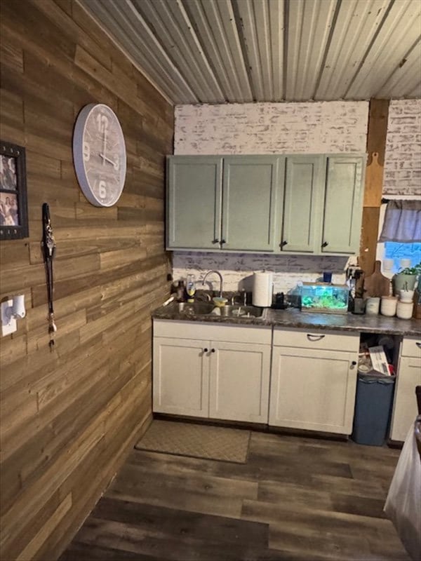 kitchen with dark countertops, a sink, wooden walls, and dark wood-style flooring