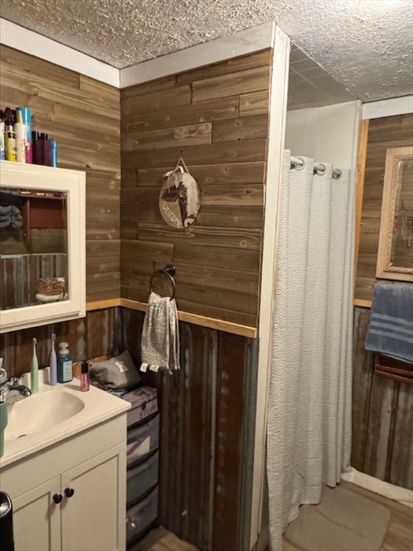 full bath with a textured ceiling, a shower with shower curtain, vanity, and wooden walls