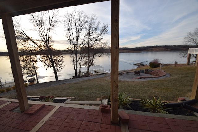 patio terrace at dusk featuring a water view and a lawn