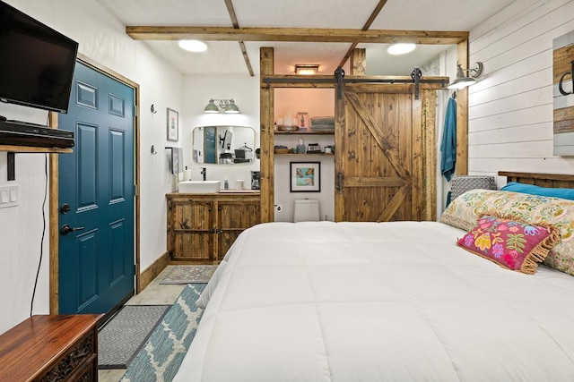 bedroom featuring beam ceiling, a barn door, and wooden walls