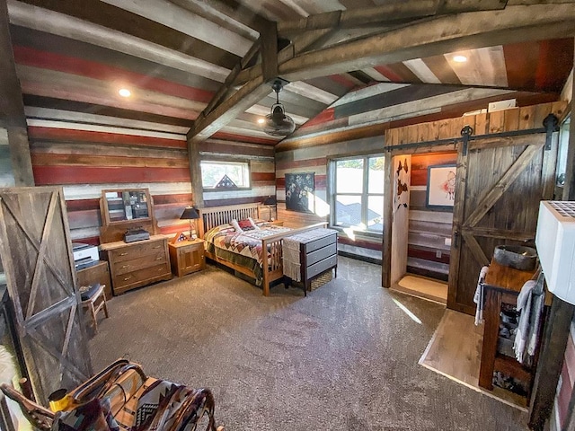 bedroom with a barn door, wooden walls, lofted ceiling with beams, and dark colored carpet