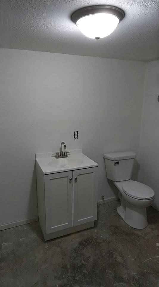 bathroom with toilet, concrete flooring, vanity, and a textured ceiling