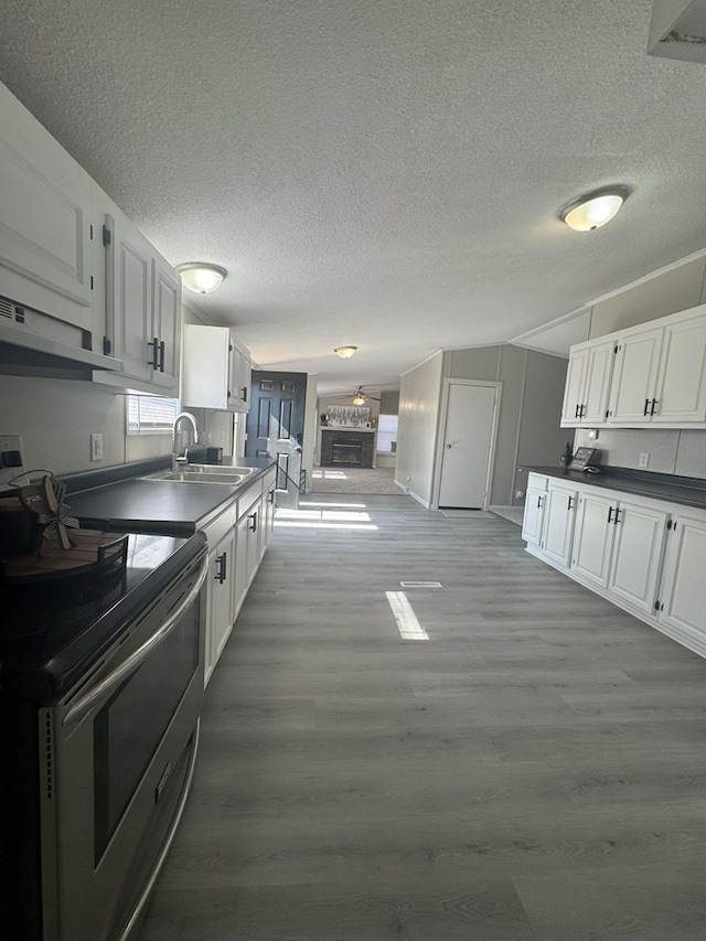 kitchen with a sink, stainless steel electric range oven, dark countertops, and white cabinetry