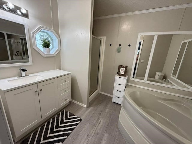 full bathroom with vanity, wood finished floors, a stall shower, ornamental molding, and a garden tub