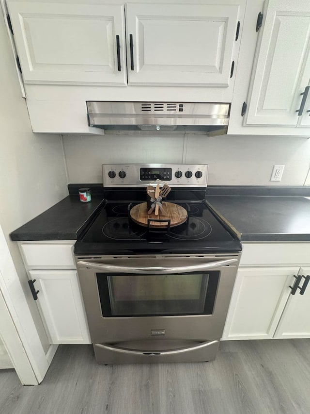 room details with under cabinet range hood, stainless steel electric range, white cabinetry, and dark countertops