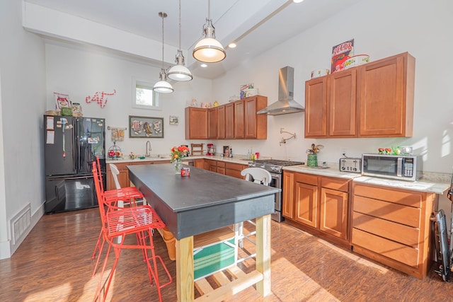 kitchen with stainless steel appliances, a sink, wood finished floors, visible vents, and wall chimney exhaust hood