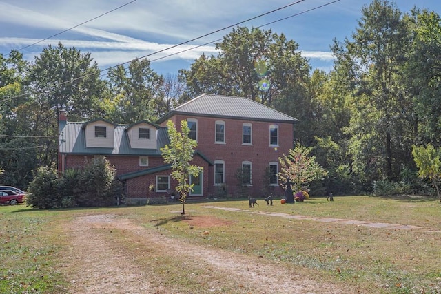 view of front of property with brick siding, metal roof, a chimney, and a front lawn