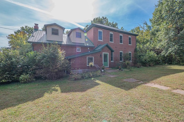 rear view of property with brick siding, a lawn, and a chimney