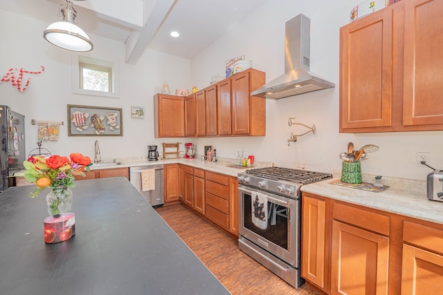 kitchen with dark wood-style floors, hanging light fixtures, appliances with stainless steel finishes, a sink, and wall chimney range hood