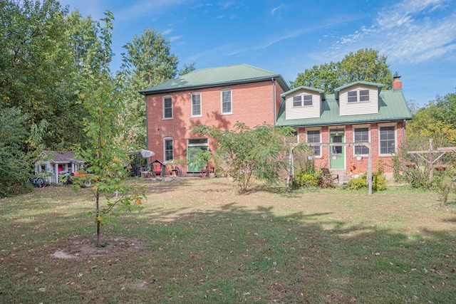 back of property featuring metal roof, brick siding, a lawn, and a chimney