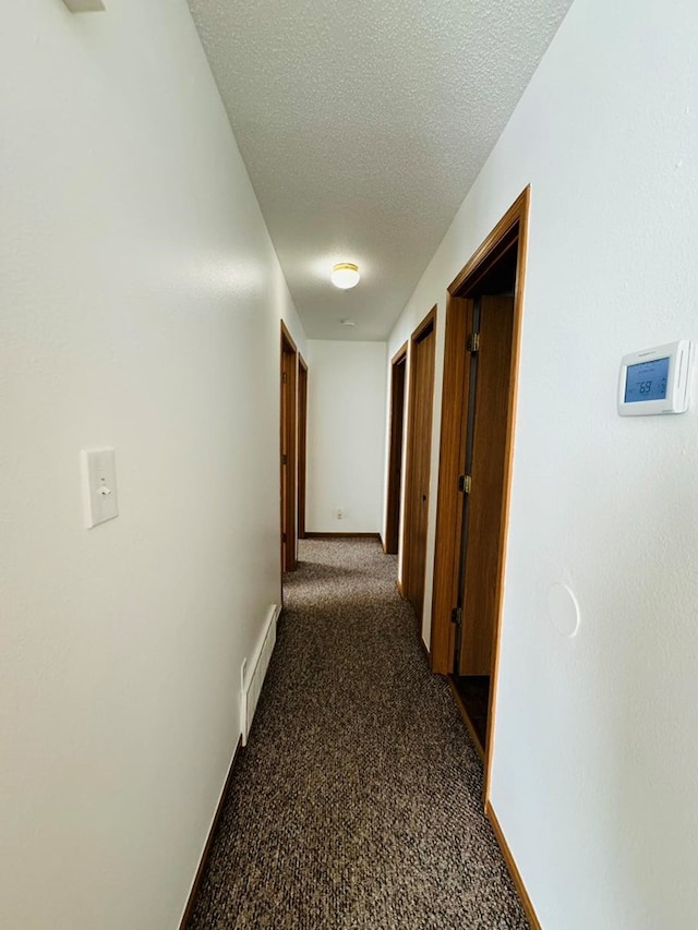 hall with a textured ceiling and dark carpet