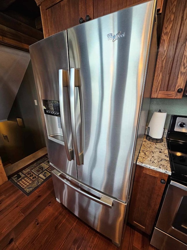 kitchen featuring light stone counters, stainless steel fridge with ice dispenser, dark wood-style flooring, and stove