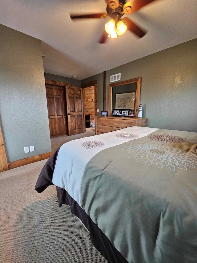 bedroom with a textured wall, visible vents, carpet floors, baseboards, and ceiling fan