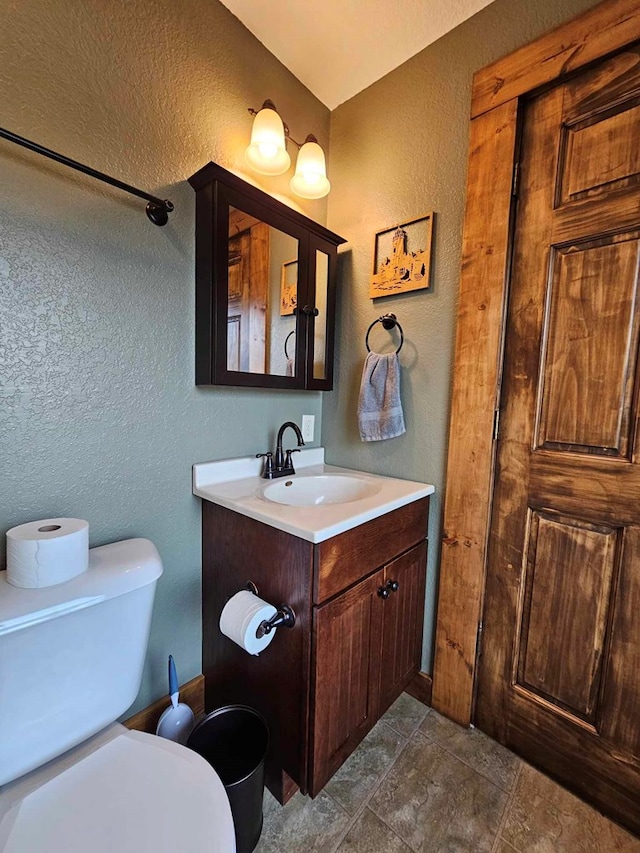 bathroom with a textured wall, vanity, stone finish flooring, and toilet