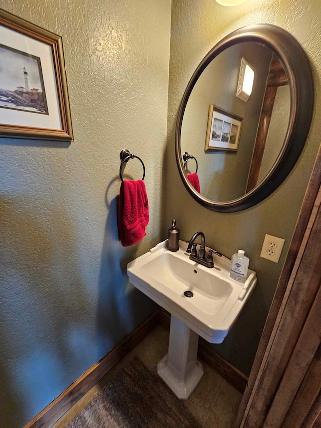 bathroom with a textured wall, baseboards, and a sink